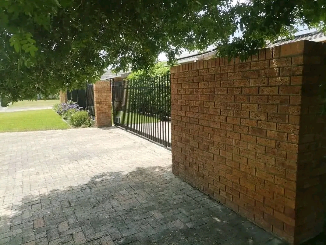 Brick boundary wall with steel gate and paving